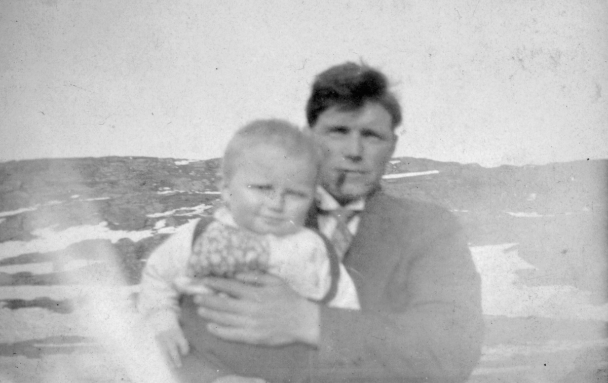 En mann holder et barn i armene. Sted og personer er ukjent, men bildet er muligens tatt i Kvalsund kommune.