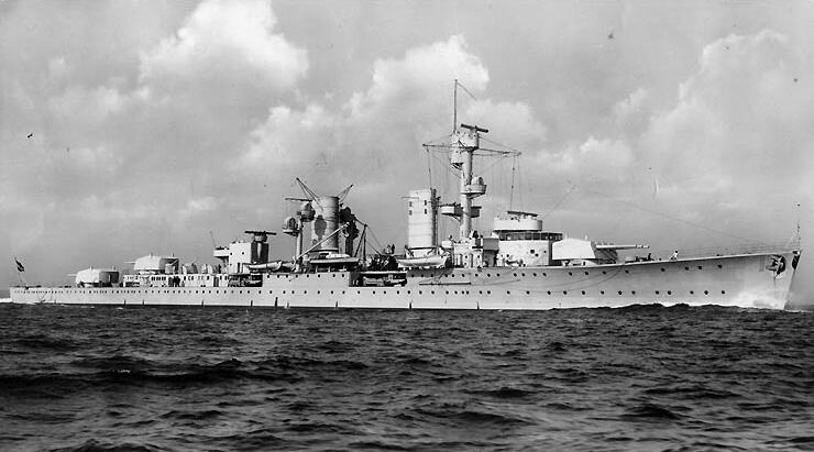 Sort/hvitt bilde av krysseren Karlsruhe på sjøen, sett fra styrbord side. Skyer tårner seg opp i bakgrunnen.