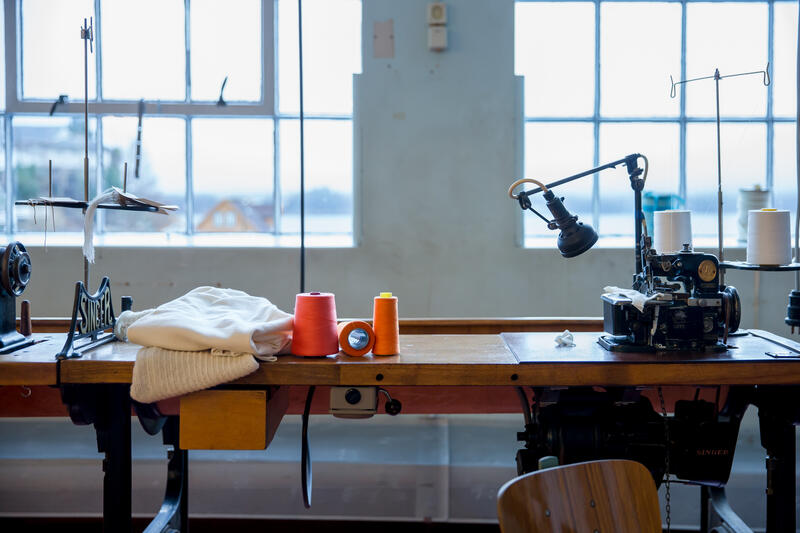 symaskin på trebord i fabrikklokale, oransje og raud sytråd (Foto/Photo)