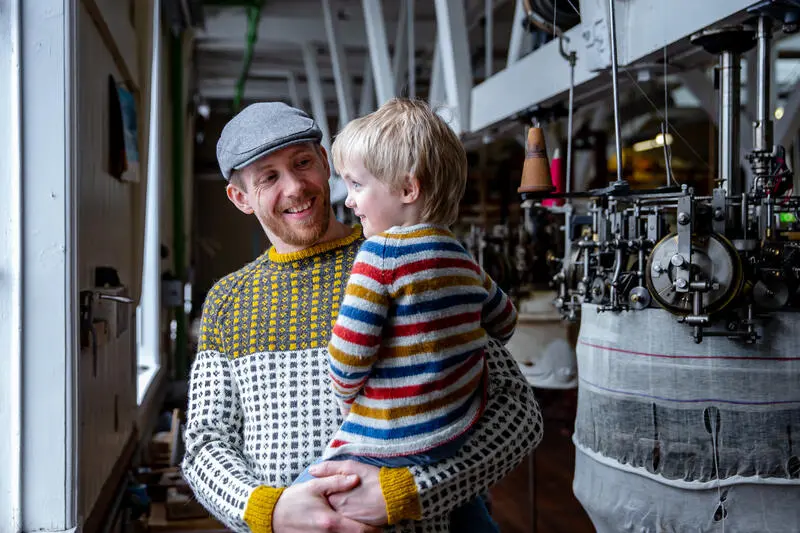 mann og barn i fabrikklokale med strikkemaskiner