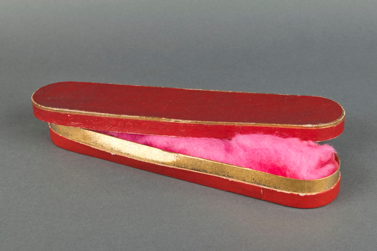 Avlang gullsmedeske med lokk. Relieffdekor på begge deler. Et stykke rosa bomull ligger i esken.
