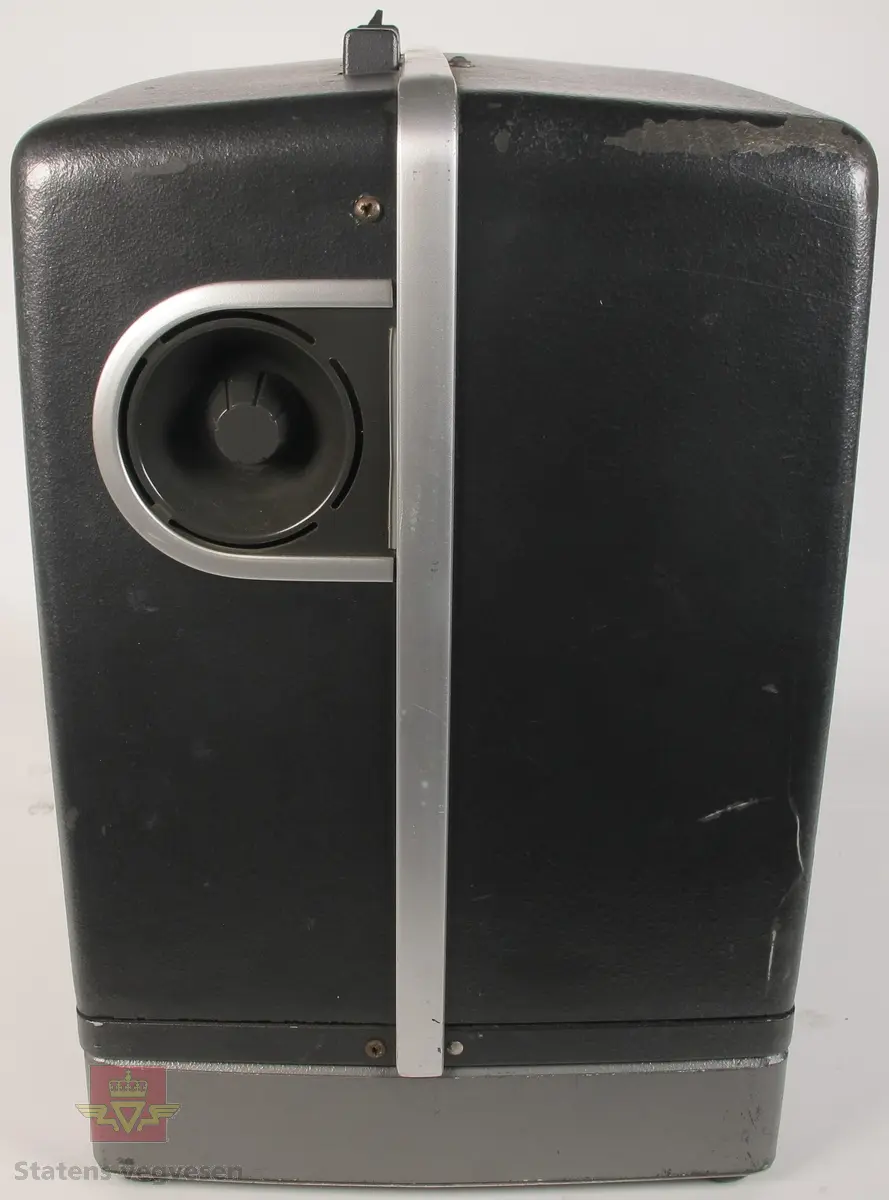BELL & HOWELL MODEL 642. 16 mm filmfremviser i mørk grå koffert av glassfiber, med defekt bærehåndtak. Den ene delen av kofferten har høyttaler av merket Goodmans, ledning for tilkobling av høyttaler og to klistremerker med påskrifter. Filmfreviseren har eget panel for justering av lyden. Bak på kofferten er det to skiltplater med innskrifter, MODEL 642 SK SERIAL No. K418 220V-1100 W - 50 ~ MADE IN ENGLAND og HANS H. KNUTSEN & CO. OSLO TYPE 642 No 418 P.VOLT 200/250 50 ~ S.VOLT AMP. 1200W. Veske, strømledning, ekstra lyspære og to tomme filmruller følger med filmfremviseren.