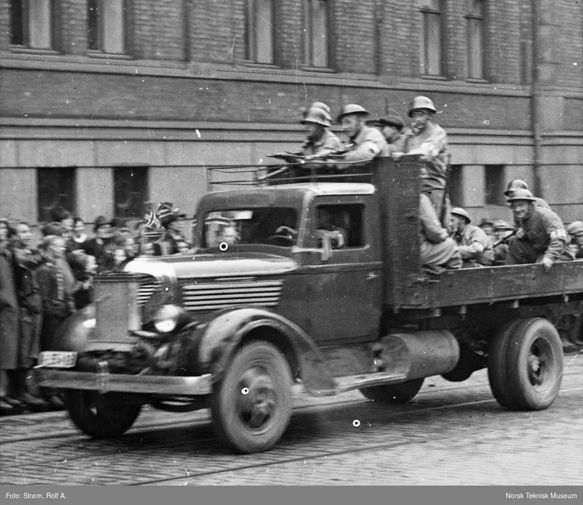 Militære på lastebil, kjører forbi folkemengde som vifter med norske flagg, Oslo, mai 1945,