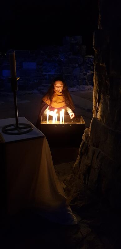 A woman in Medieval costume is lighting candles in the ruins of Hamar cathedral.