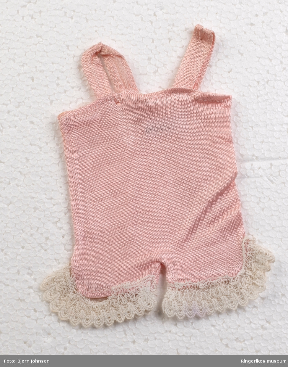 Hjemmesydd rosa seleshorts i polyester. Påsydd hvite blondebånd på beinkantene. Reparert med håndsøm og hvit tråd på baksiden.