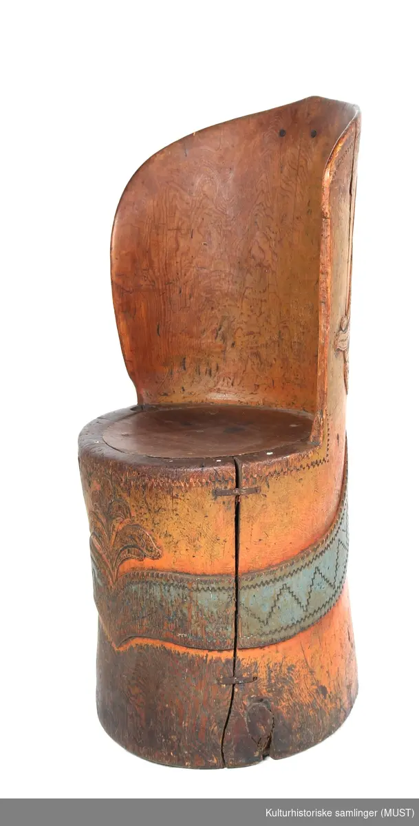 Rødmalt kubbestol med blått ,sikk sakk mønstret bånd rundt stammen. 
Ryggens bakside er dekorert med akantusblader. 
Akantusdekor i forkant.
I stolens sete er det slått inn tenner.