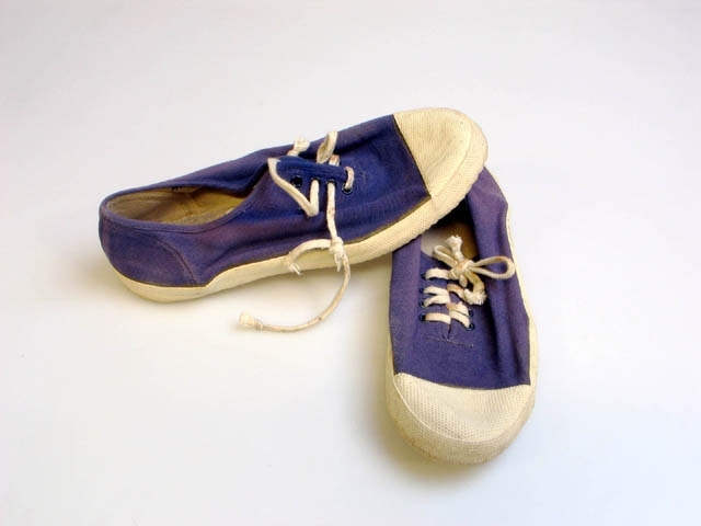 Ett par blå tygskor med vit tåhätta av gummi och vit gummisula. Skorna har vita skosnören. Skorna har varit utställda i basutställningen "I barnaminne" på Landksrona museum. Utställningen stod mellan 1989 och 2007.