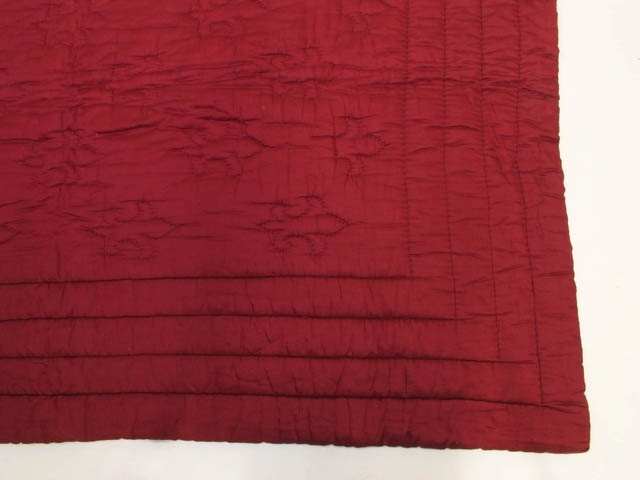 Rött täckstickat täcke med ljusgul undersida. Dekorerad med två versioner av täckstickade franska liljor.