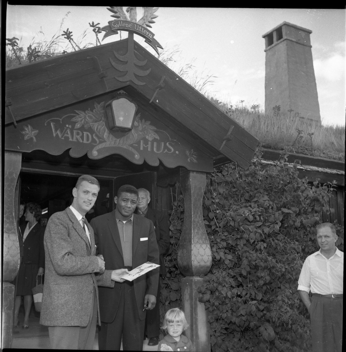 Två män står vid entrén till restaurang/hotell Gyllene Utter. Mannen till vänster är ägaren Rolf von Otter som håller den autograf han just fått av den andra mannen, boxaren Floyd Patterson.
