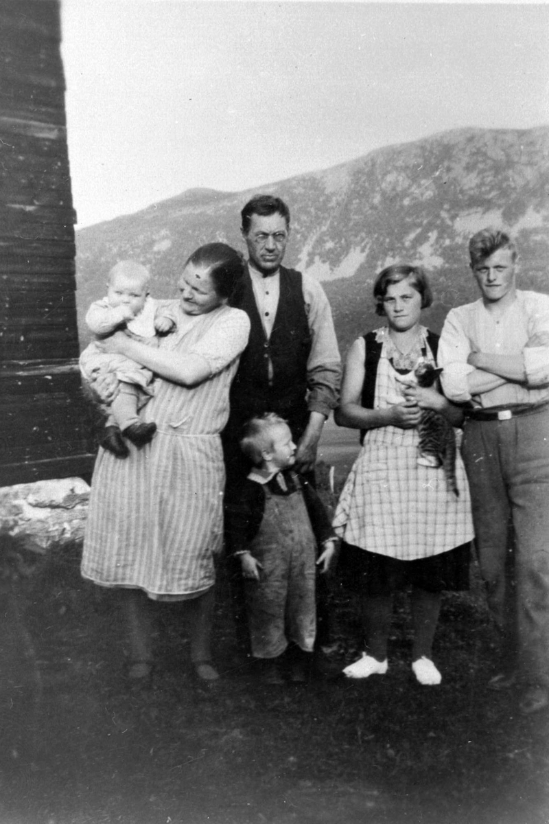 Gruppebilde av fire voksne med to barn stående ved husvegg i Tømmeråsen.