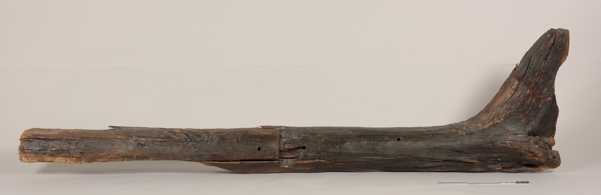 Stevn av båt av treverk, med fem hull for jernbolter. To jernbolter bevart.  Merket med tusj som "III-23".