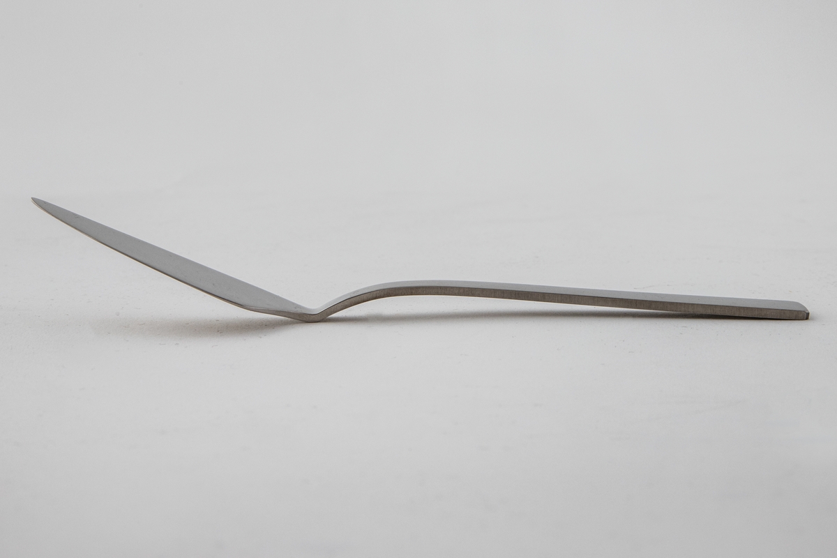 Liten serveringskniv i polert, rustfritt stål. Bladet danner en butt vinkel fra det rettlinjede skaftet. Sistnevnte er mattert, mens bladet er polert, slik at det oppstår en kontrast mellom de blanke og matte partiene.