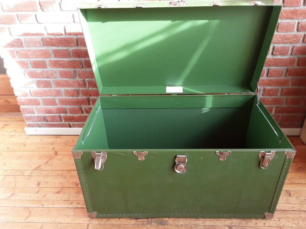 Koffert dekket med grønn vinyl, kantene forsterket med bånd og hjørnene med metallbeslag. Lærhåndtak på hver kortside.