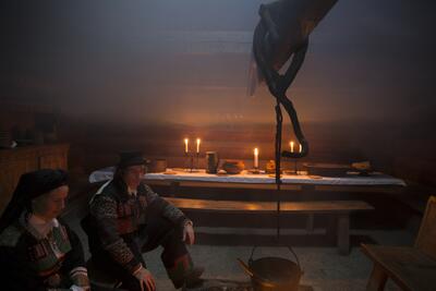 En kvinne og en mann sitter foran bålet i årestua. I bakgrunnen et julepyntet bord.. Foto/Photo