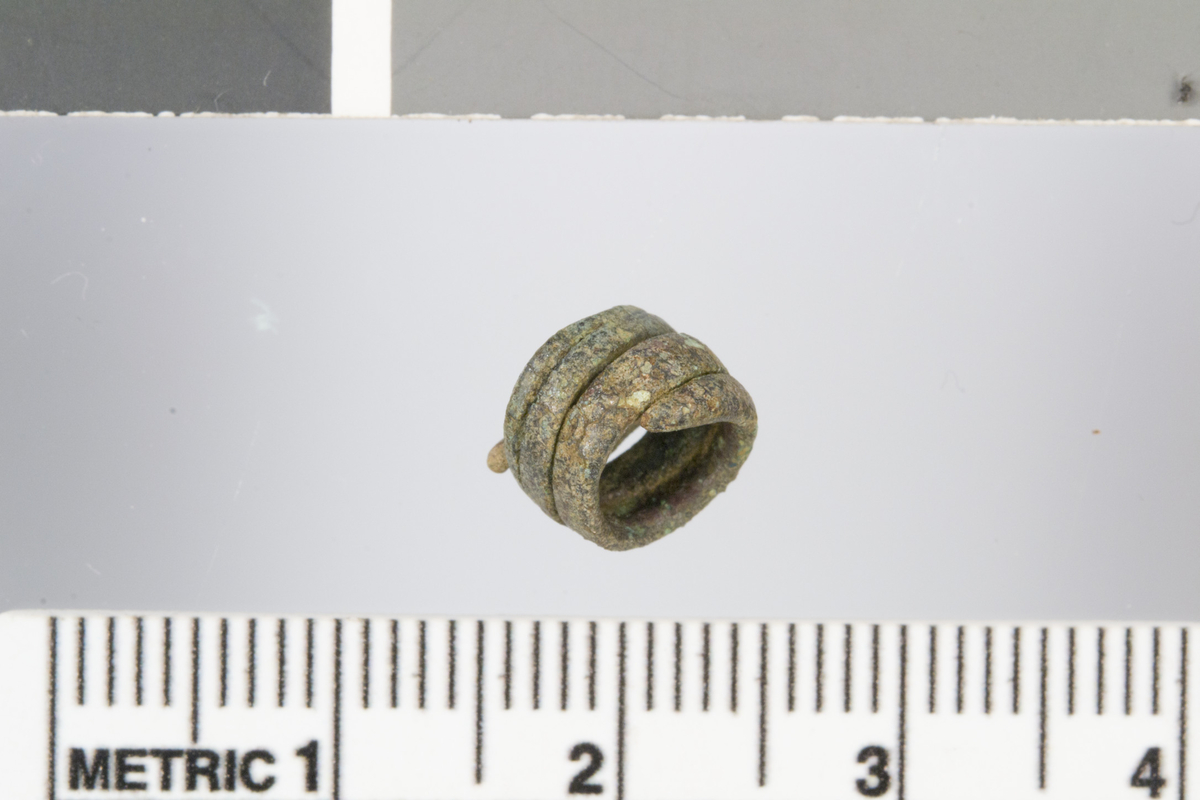 Liten spiral i bronse. 0,7 cm i diameter og 0,5 cm høy. Funnet ved skår av den udekorerte urnen (unr.2).
