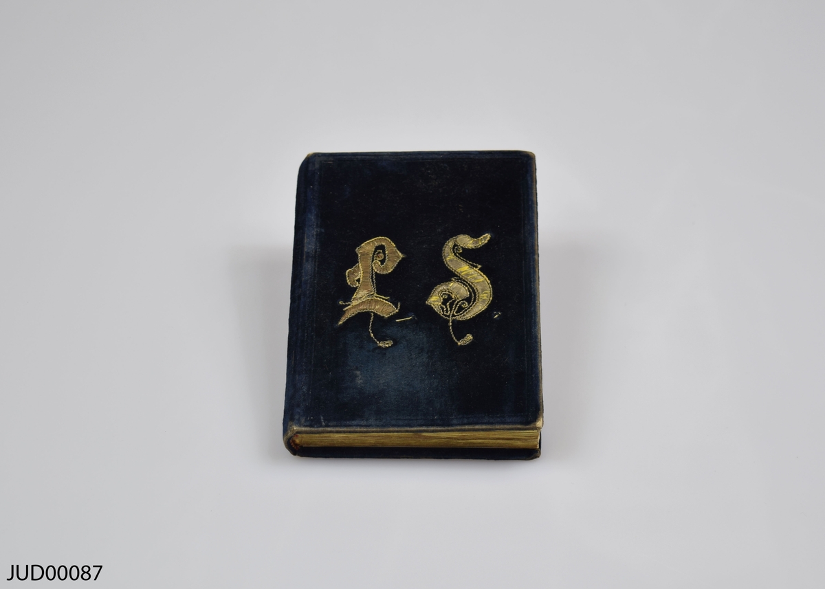 Bönbok med mörkblått sammetsomslag. Dekorationer utförda med guldtråd i form av initialerna LS på ena sidan, och en harpa på andra sidan.