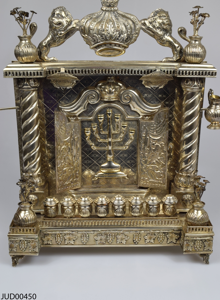 Chanukaljusstake tillverkad av silver med oljehållare, blomsterdekor och krona flankerad av lejon.