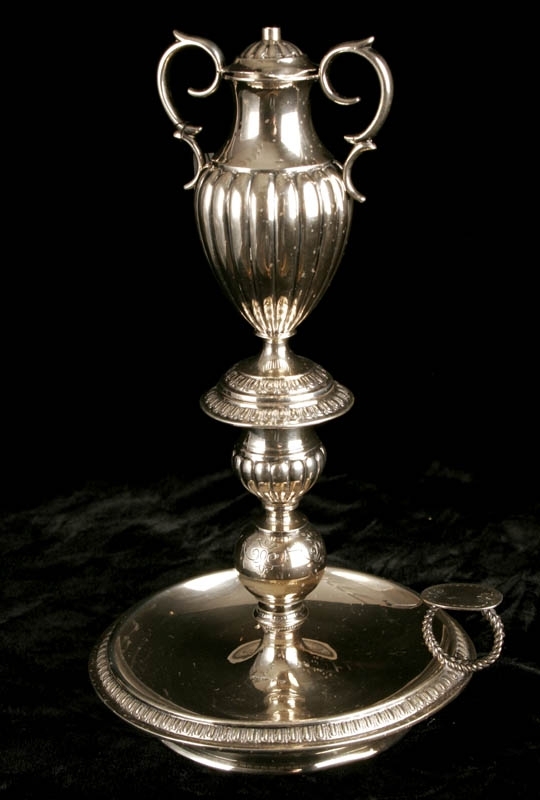 Årslampa. Svensk silverljusstake i tre delar. Toppen är i form av en amfora med handtag och lock. Ristade årtal på amforan - 1829, 1894 samt 5655.