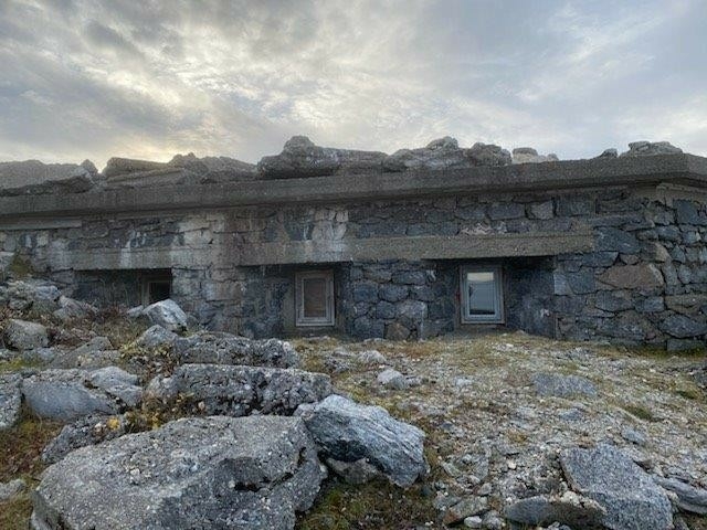 Kommandobunkeren ligger i landskapet. Den er bygd opp av stein og betong, med 
vinduer mot sjøen.