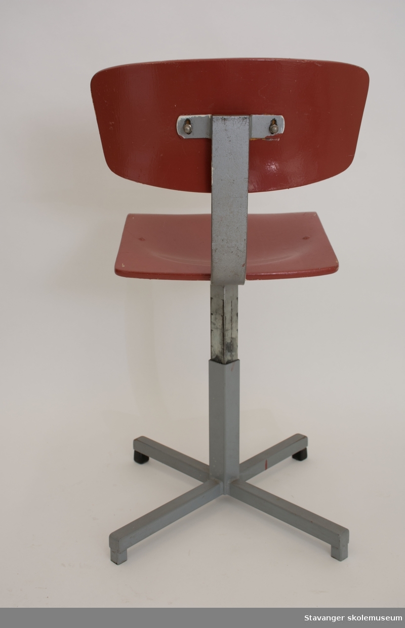 Elevstol av jern og bøyd kryssfiner. Gråmalt st]l og rødmalt kryssfiner i sete og rygg. Er justerbar i høyde.