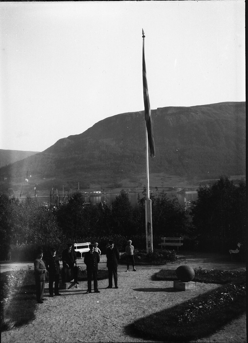 Okända män och några pojkar samlade i en park vid en hissad flagga.