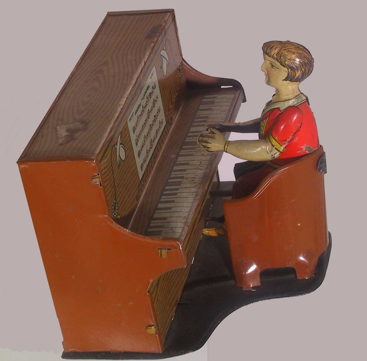 Piano med stol foran, i denne sitter en pianist. På baksiden av pianoet en sveiv som lager lyd og beveger pianisten.
