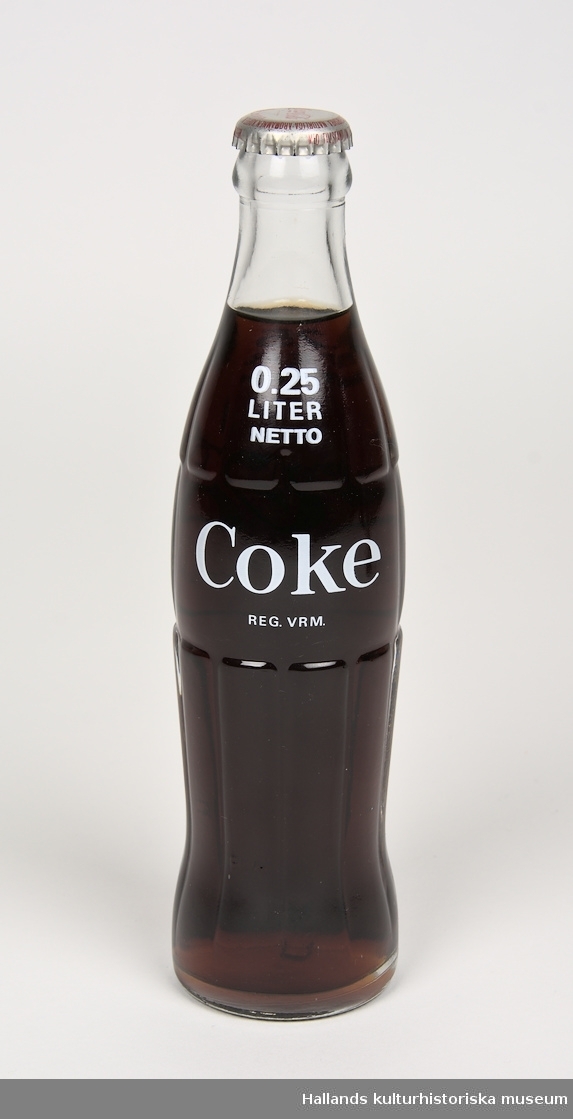 Läskedrycksflaska: Coca-Cola. Flaskan är tillverkad av klart glas. På flaskans bröst finns ett vitt tryck i form av en "Coca-Cola"-logotyp samt text. 250ml. Oöppnad.