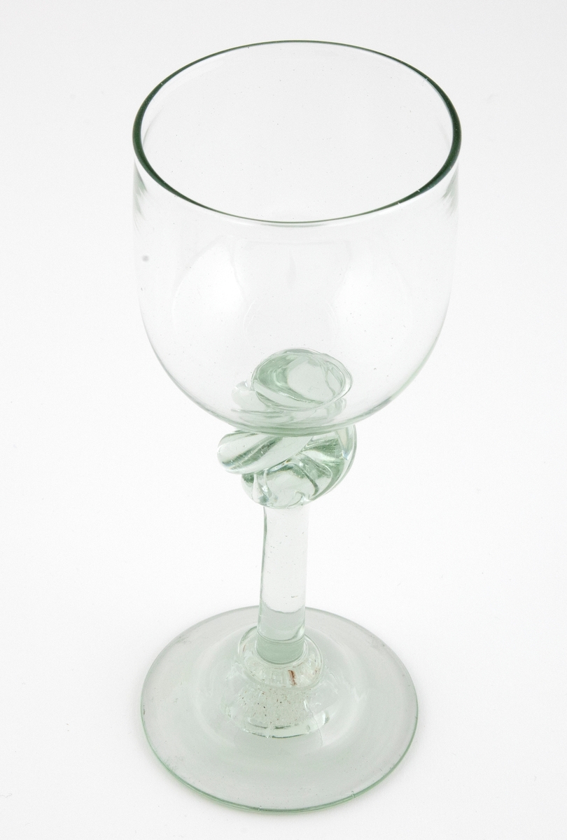 Drikkeglass i klart grønntonet glass med klokkeformet kupa, som hviler på en tynn stett med spiralformet vulst. Rund fotplate, noe opphøyet i midten.