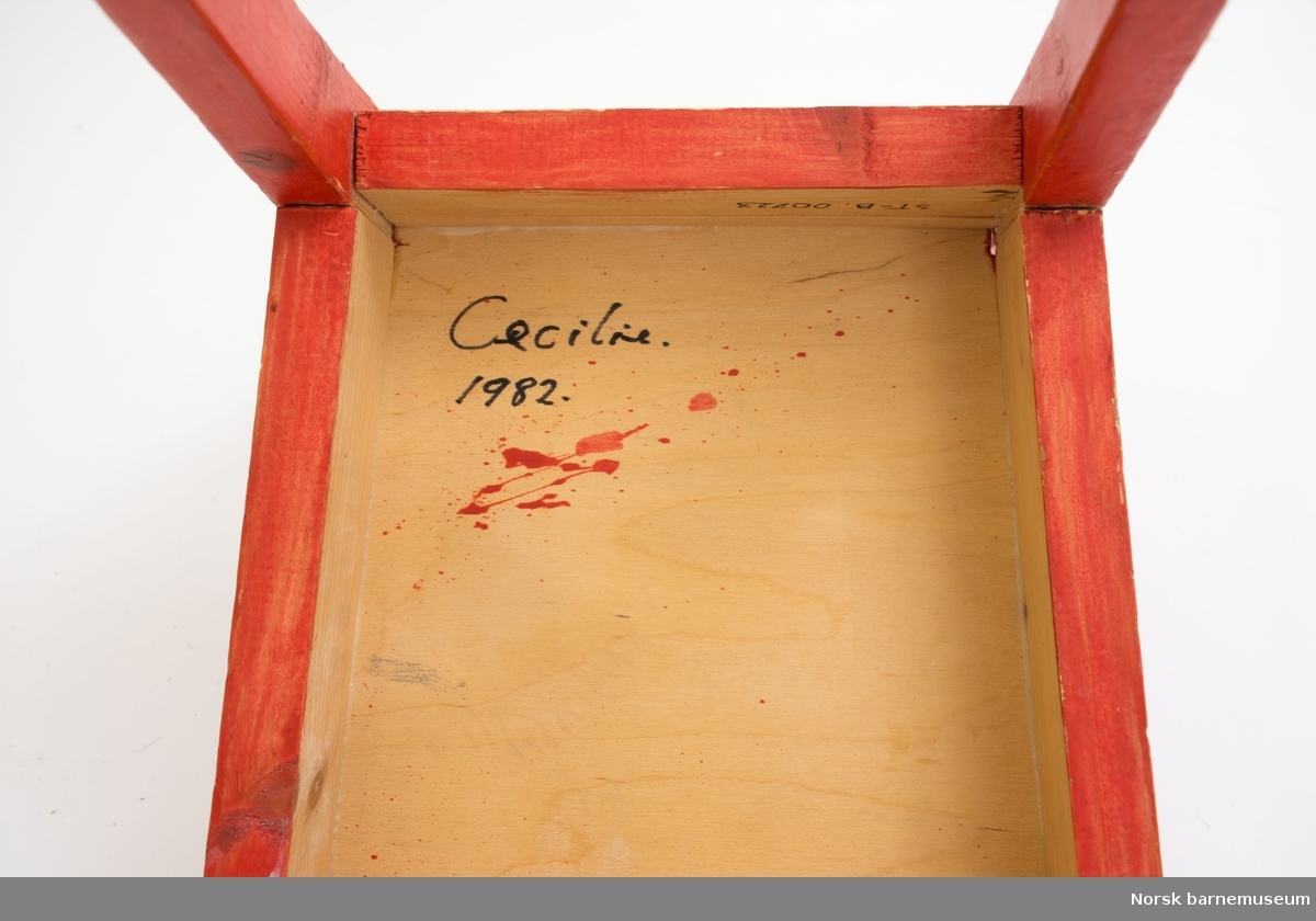 Rødmalt hjemmelaget furustol med klistermerker og påskrift "Cecile, 1982". Kryssfiner av bjørk i sete. Reparet i akterstavene.