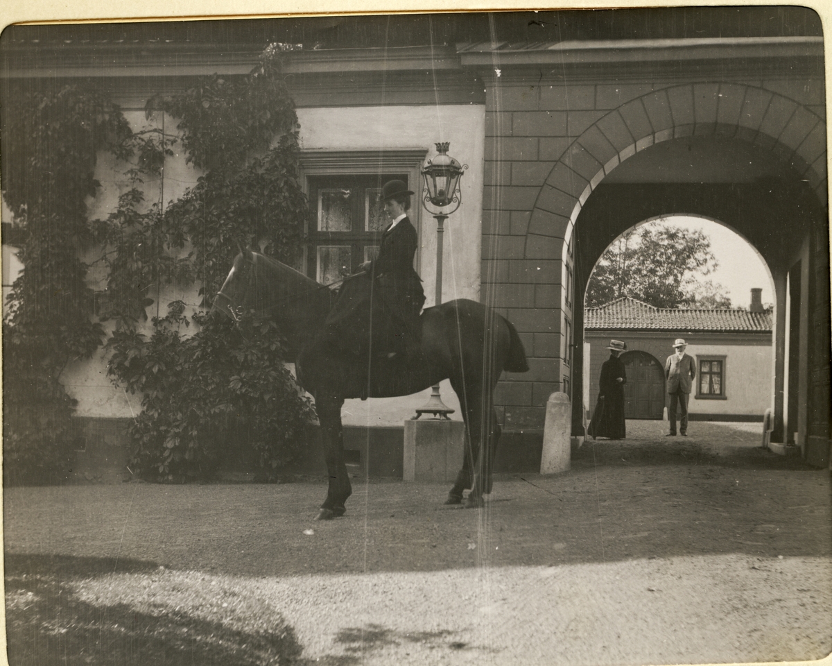 Nini Egeberg på hesten "Aiglon" ved inngangsporten til Bogstad gård. Hennes foreldre Mathilde og Herman Wedel Jarlsberg står i portrommet. Fotografert september 1909.