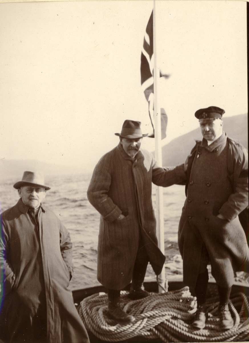 Medlemmer av Christiania Tømmerdirektion står i akterstavnen på en båt. Fra venstre Otto Nielsen (I.N. Jacobsen & Co), fløtningsdirektør i Nedre Glommen W. Blakstad og Westye P. Egeberg. Fotografert 1915.