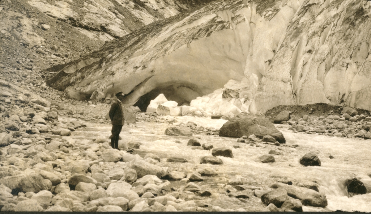 En mann  i sjåføruniform( Bogstads Kristian Skuggen?), står ved en isbre, trolig i Loen i Sogn og Fjordane. Fotografert 1923.