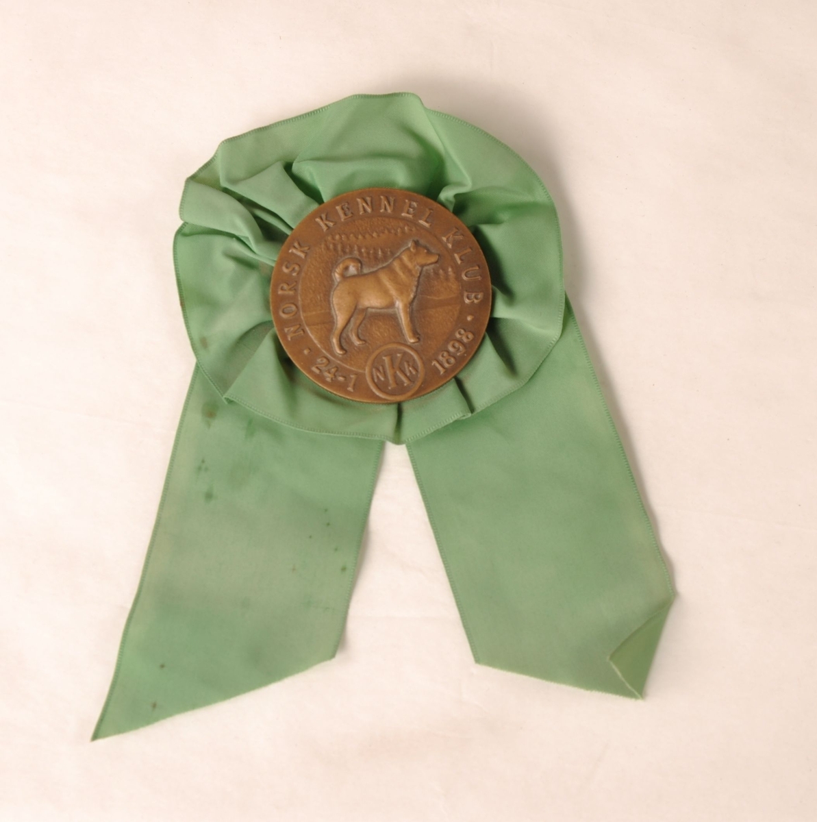 Rosett av grønt tekstil med medalje av brunt metall i midten.
