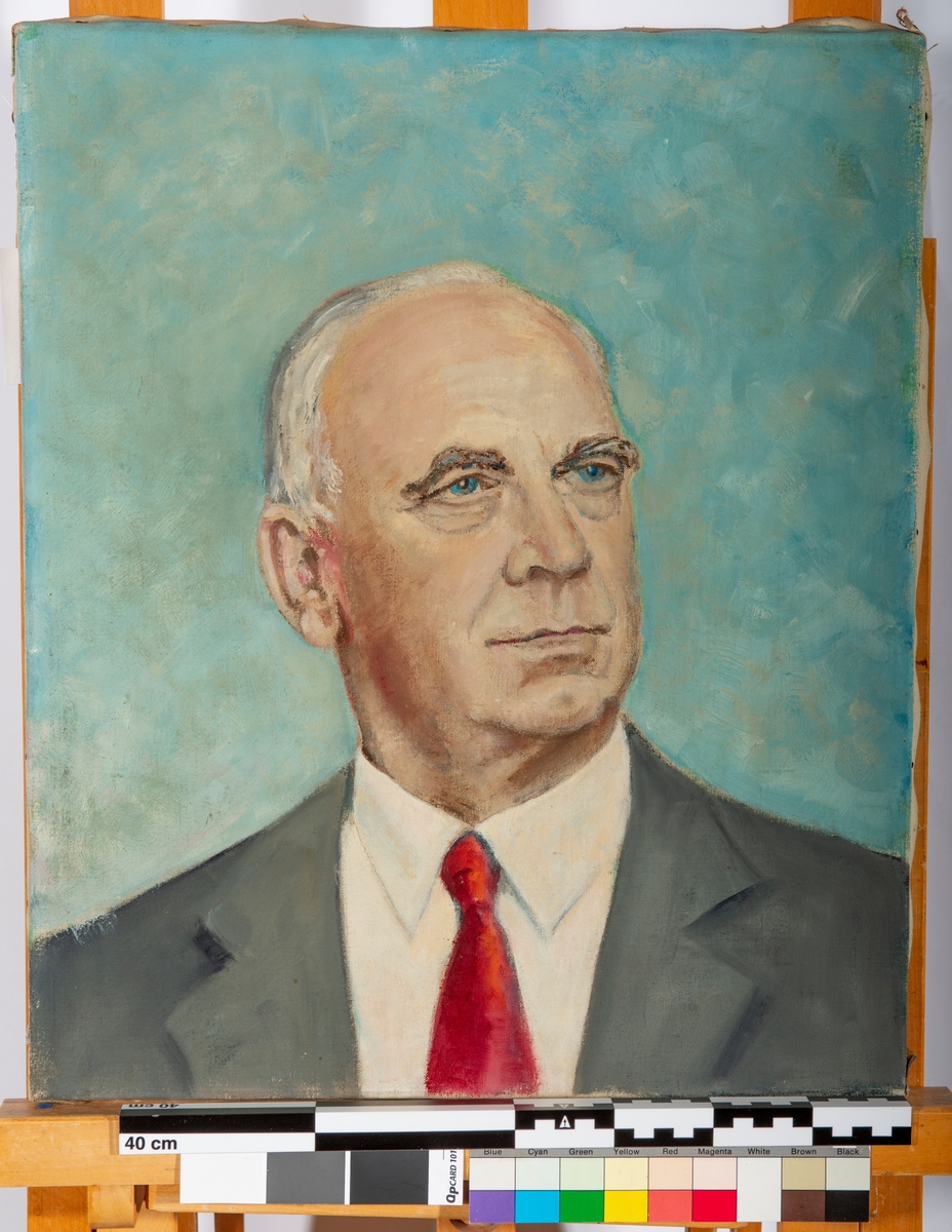 Portrett, Brystbilde, trekvart profil vendt mot høyre. Kledd i hvit skjorte, rødt slips og grå jakke. Blålig bakgrunn.