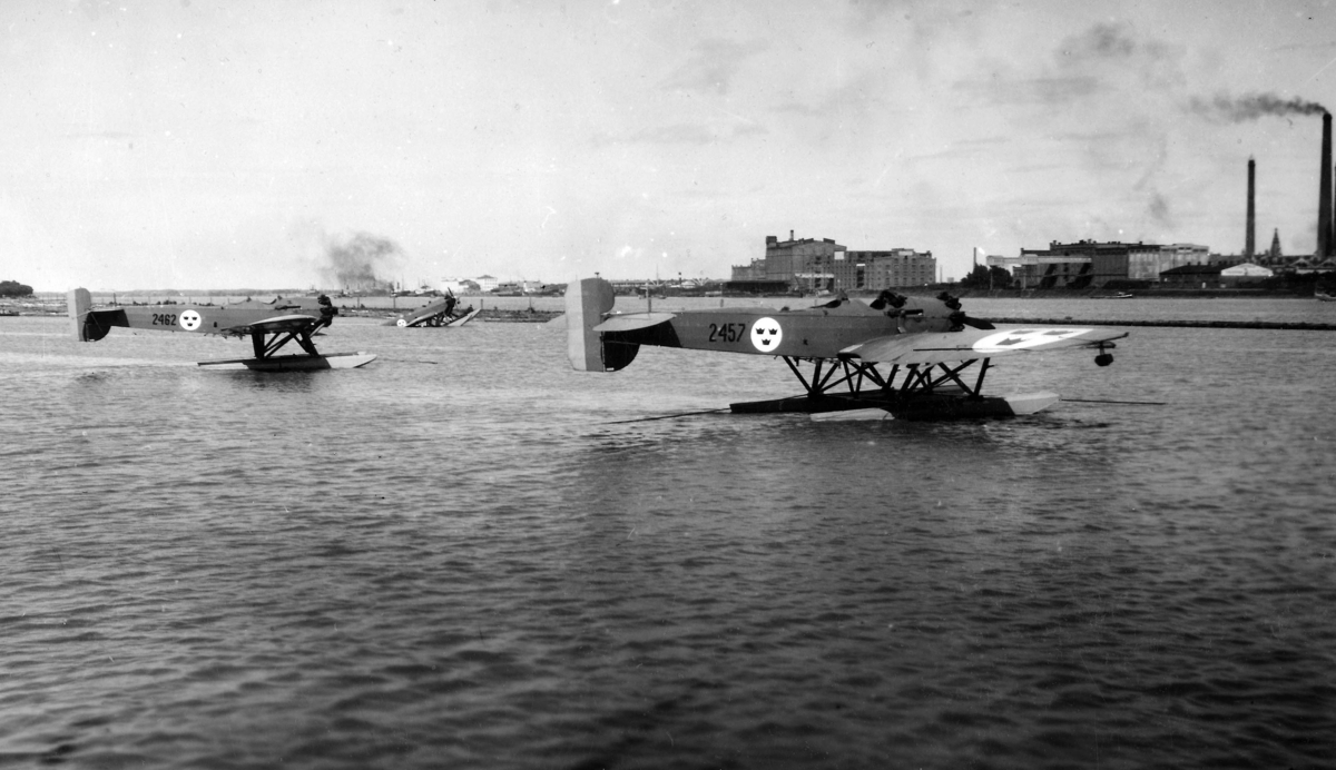 Tre flygplan S 5 på vatten med stadsmiljö i bakgrunden. Två av flygplanen är märkta med nummer 2457 respektive 2462. Det tredje flygplanet, nummer 2451 har sjunkit. 1930-tal.