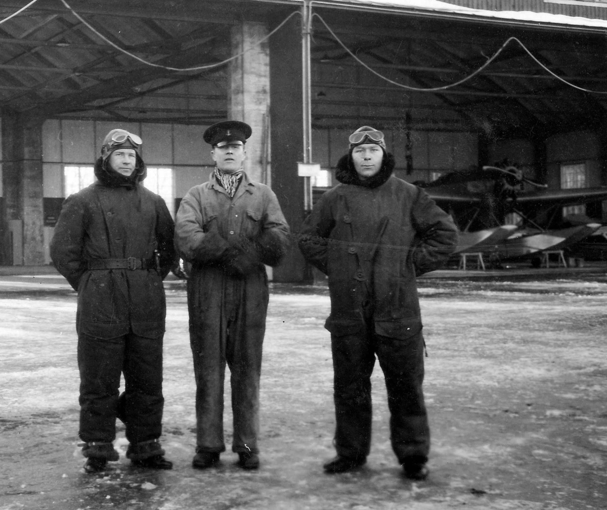 Porträtt av tre soldater vid F 2 Hägernäs, vintertid. Två av männen är klädda i flygardräkt. Hangar i bakgrunden. 1930-tal.