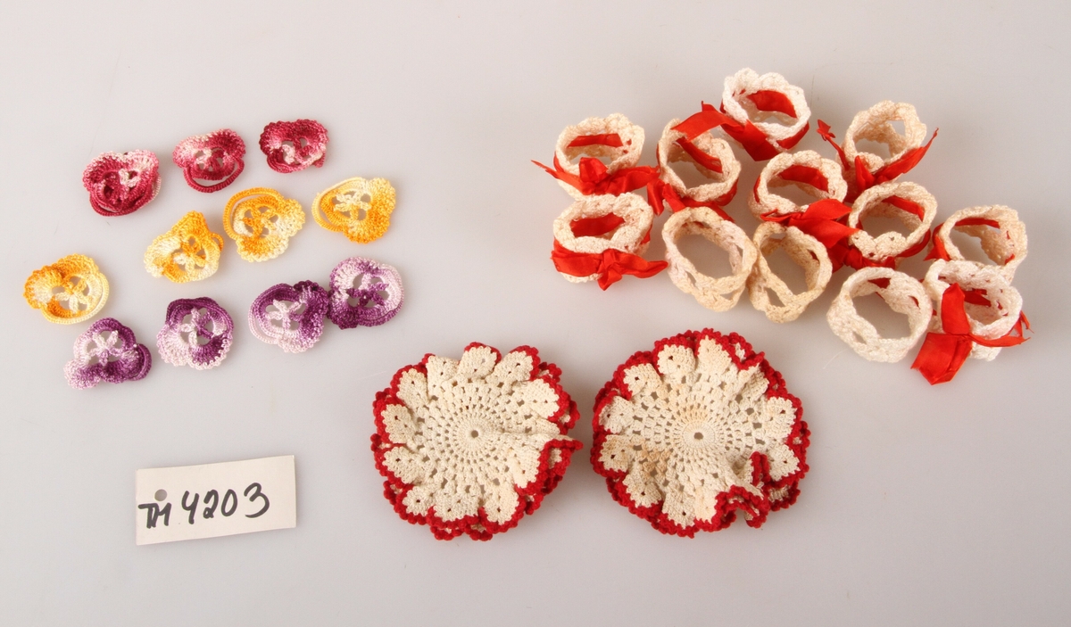 Ulik hekling - 12 kvit heklete serviettringer, 9 av dem med silkesløyfe, 12 heklede blomster i ulike farger og to kvite brikker med rød kant. 