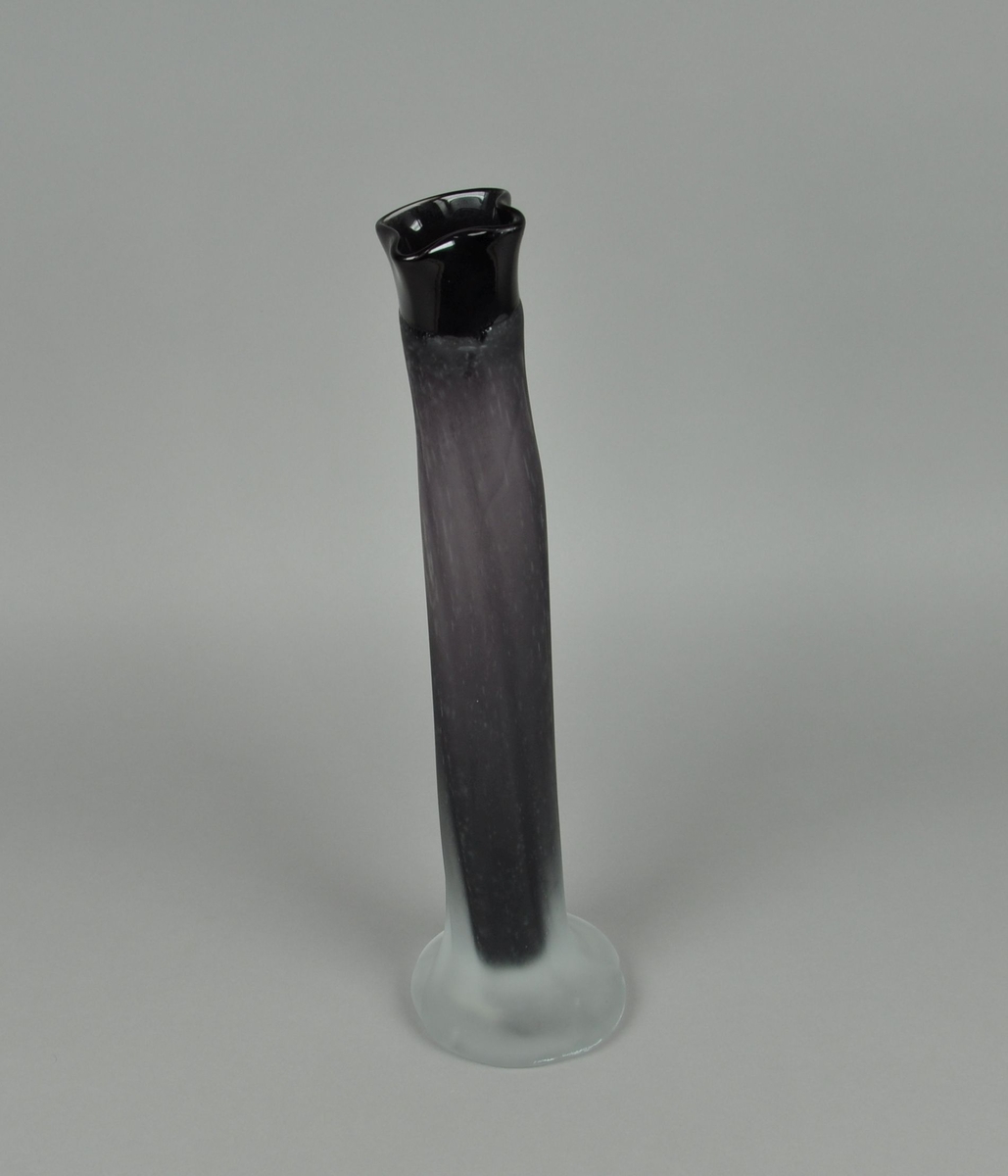 Munnblåst vase av glass. Sylindrisk form, med bølgete form øverst og utvidelse til sokkel nederst. Vasen er blåst med lilla glass med klart overfangsglass. Overflaten er frostet.