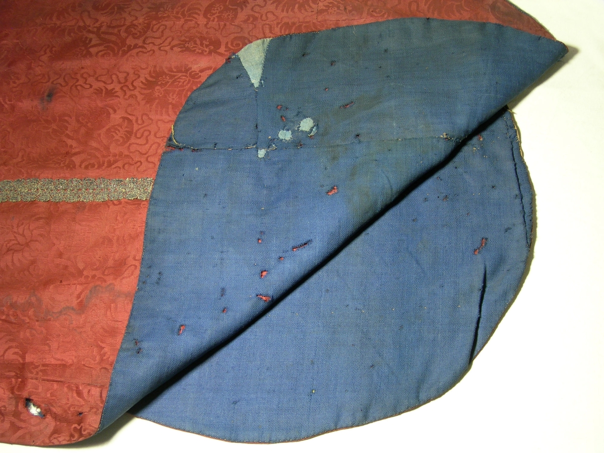 Sidendamast i 5-skaftad satin, röd.
Varp: rött silke, ca 40 tr/cm
Inslag: rött silke, ca 26 tr/cm
Blad- och blommönster omgivet av mjuk slinga.
Yllefoder i liksidig kypert (2/2), blått. Fodret lagat på några ställen med blått linnetyg, tuskaft.
Mässhaken har axelsöm och är sydd av flera stycken.
På baksidan 695 x 420 mm högt applicerat kors av 2 spetsar i metalltråd (spunnet lan, silver; lan, silver), tillsammmans 30 mm breda.