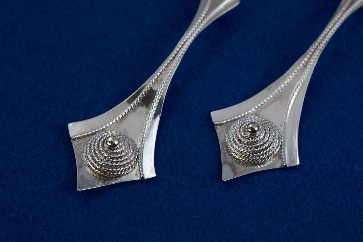 Örhängen i silver tillverkade av Rosa Taikon. De är dekorerade med en för Taikon karaktäristisk form: en spiral av filigrantråd omgärdar en minimal granalie av guld i spiralens mitt. De två örhängena har olika årsstämplar: F10 för 1980 respektive B11 för 2000.