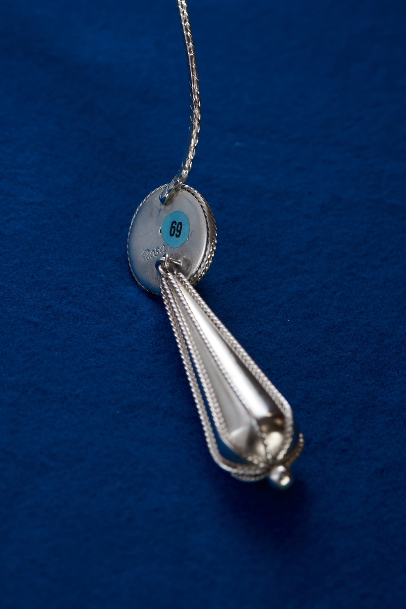 Silversmycke i filigranteknik av Rosa Taikon. Tunga, droppformade örhängen är vanliga smycken hos flera romska grupper. De kan vara utförda i såväl solid som genombruten form. Ofta bärs tyngden upp av en tunn kedja som läggs runt örat för att avlasta örsnibben. I det här huvudsmycket har Taikon valt att istället låta tyngen bäras av huvudet genom att fästa hängena i ett diadem av filigran.