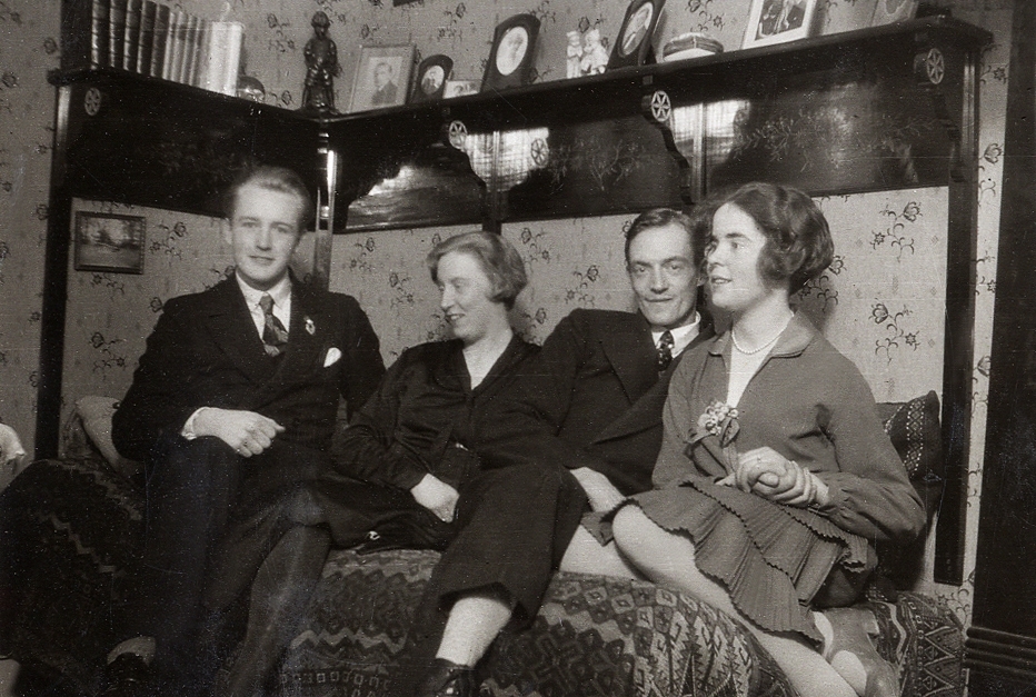Två kvinnor och två män har slagit sig ner i en panelsoffa. 
Vid fotot text: "Hos Hugo A. 1930".