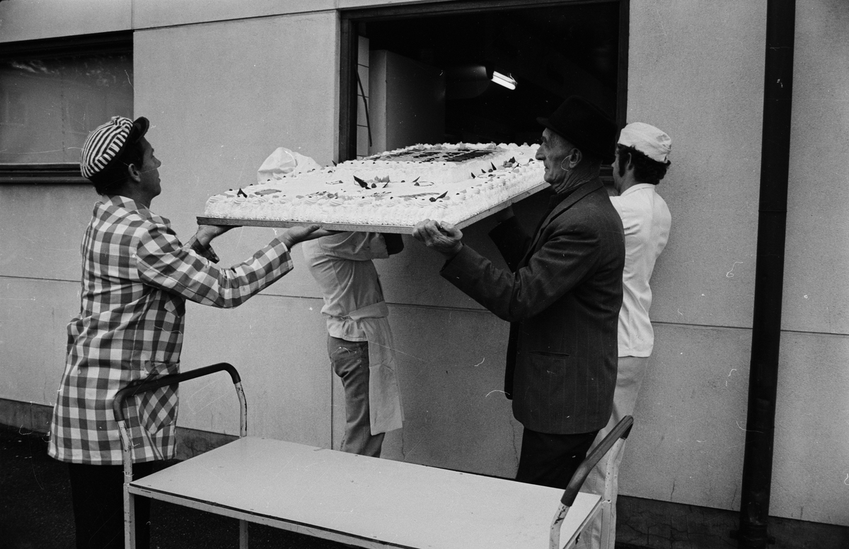 Tårtan tas ut genom ett av konditori Royals fönster. Affärsföreståndare Lars Olsson, Holger Pettersson och Kåre Lovinger eller Bernt Söderlund tar emot