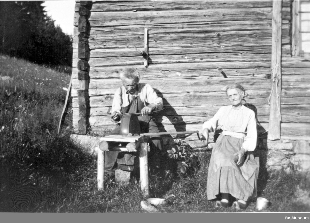Svein Holet og Ingrid Sletteli brynar ljåen ved stuguveggen i Sletteli