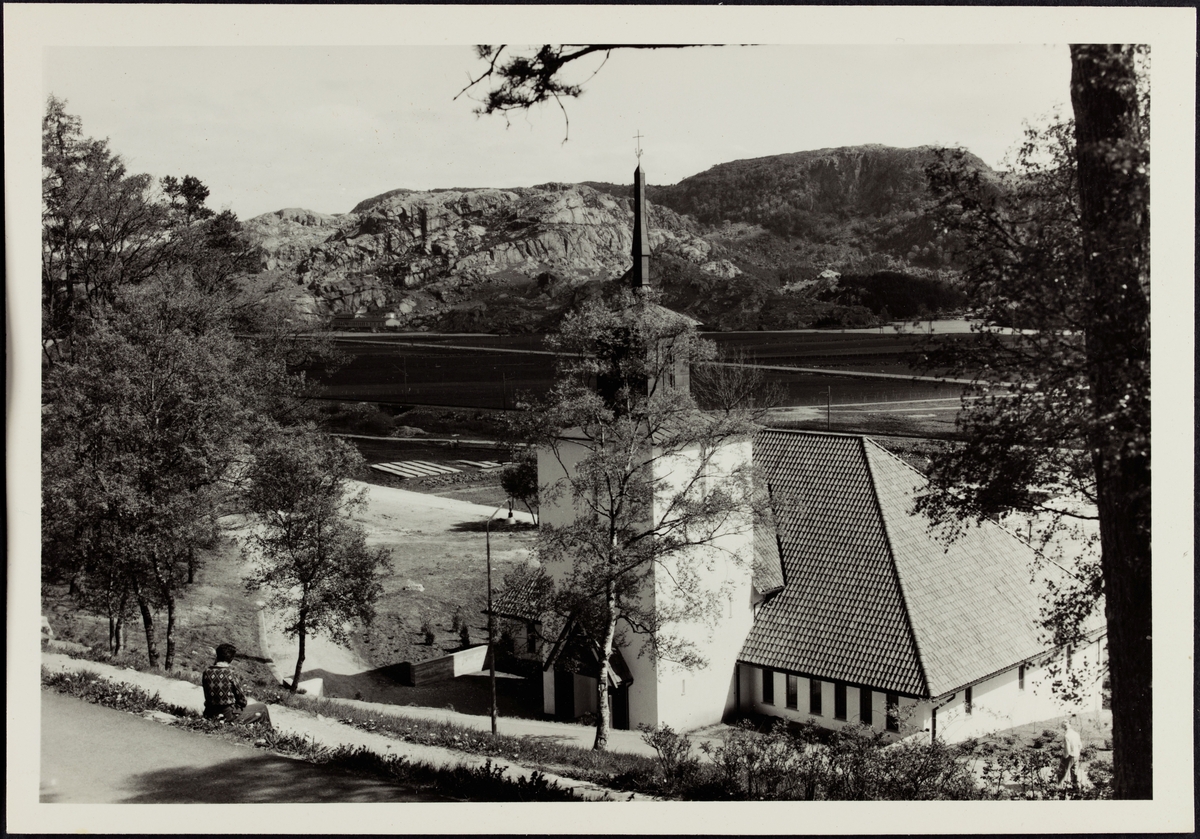 En person sitter i bakken ovenfor Bakkebø kirke i Egersund og ser utover.