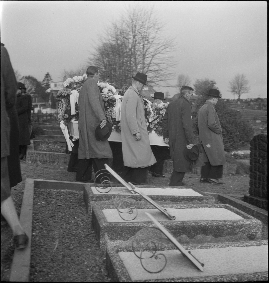 Begravelsen til fru Karlsen. En blomsterkledd kiste bæres ut og jordlegges på kirkegården i Egersund.