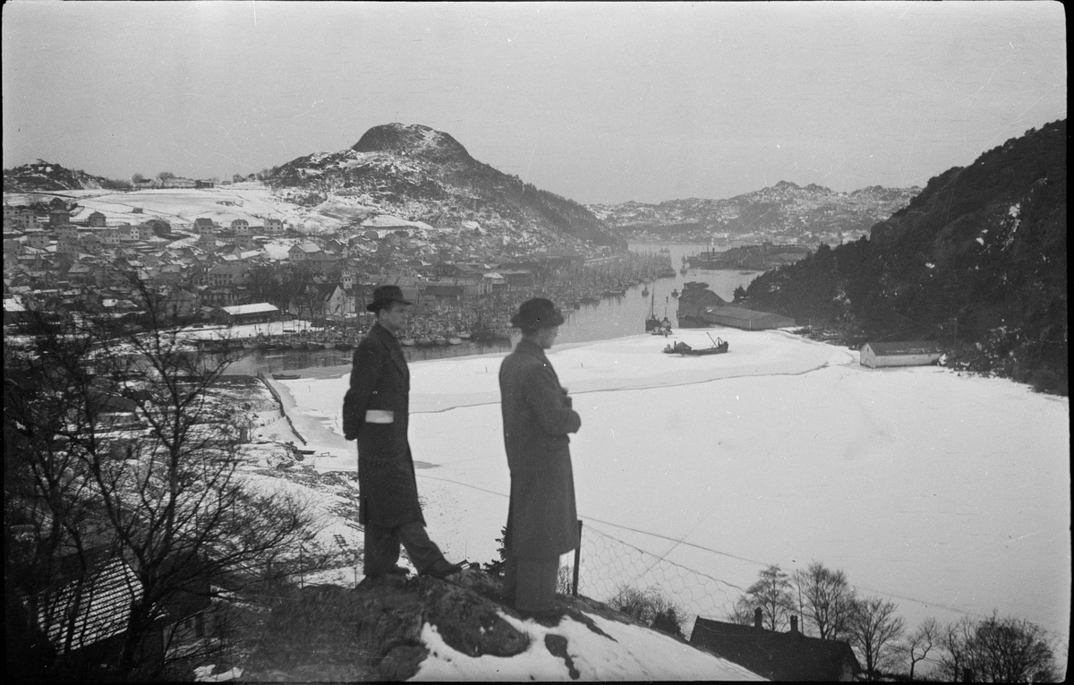 Utsikt over Vågen og Egersund en vinterdag. Det fiskeflåten ligger til kai og den innerste delen av Vågen er islagt. På bilde nr. 3 ser to menn ut over byen.