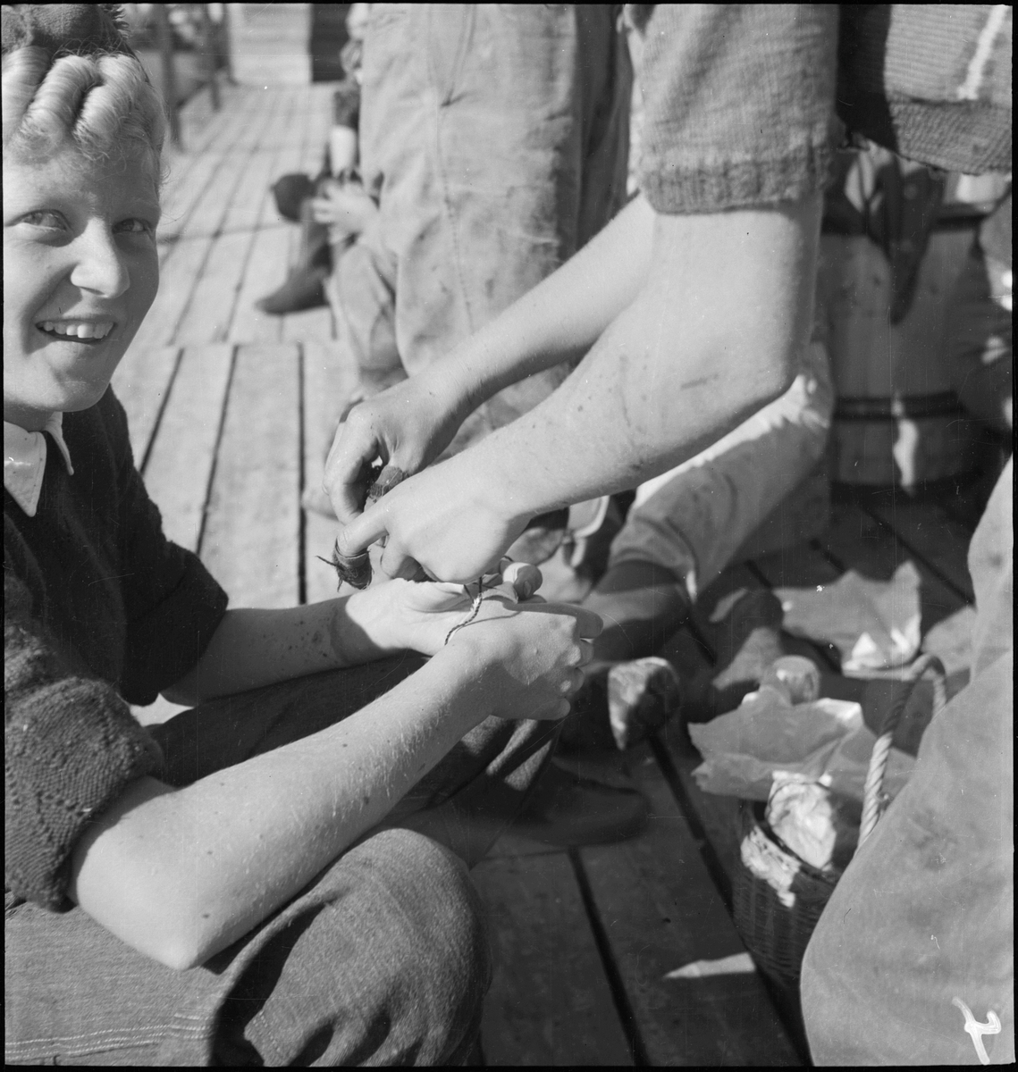 Kvinner fra et arbeidslag for mottak av makrell under en pause i arbeidet. Flere av kvinnene har polstringer rundt fingrene og håndleddene.