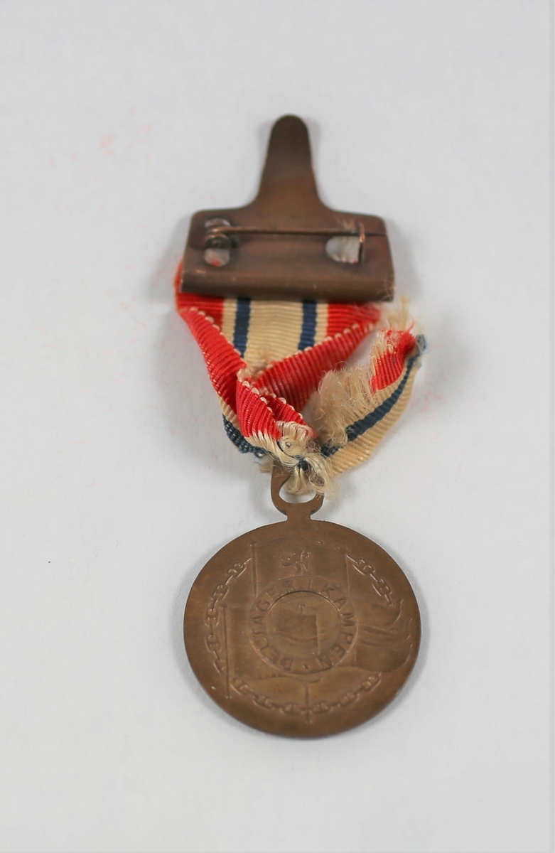 Medalje i bronse, på advers med omskriften "*9 april 1940 * 8mai 1945", riksvåpnet midten. På reversen er kongeflagget, handelsflagget og orlogsflagget. Over disse en smal sirkel med innskriften «DELTAGER I KAMPEN». Motivet er omgitt av en lenke. Båndet er delvis i dårlig forfatning og det har et lite hull midt på. Det kan tyde på at medaljen har blitt tildelt med rosett. Det vil si gitt til [..personell som tilfredsstiller kravene for krigen i Norge 1940, (og som) senere har tjenestegjort i de væpnede styrker utenfor landets grenser..]