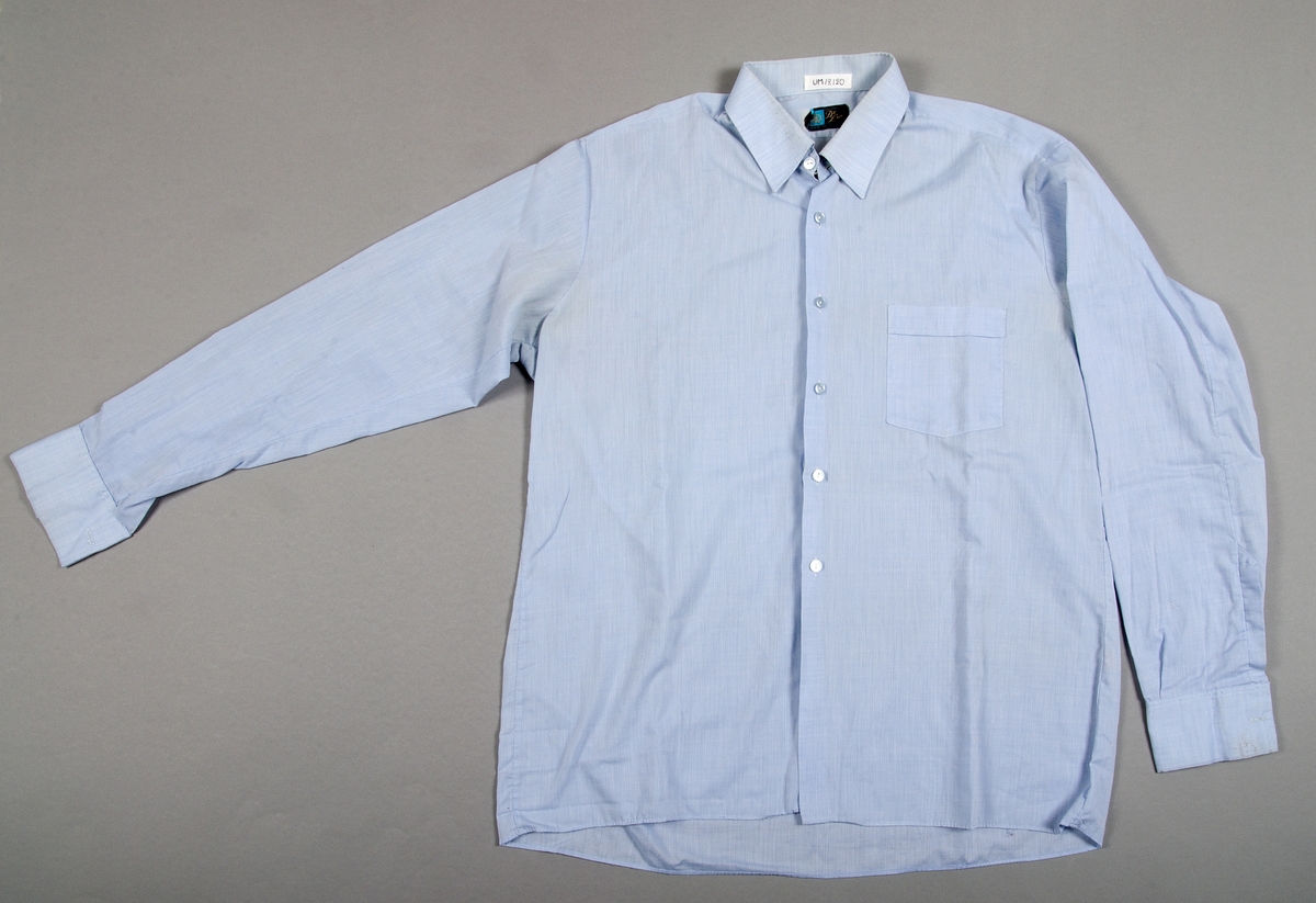 Skjorta med randig struktur av ljusblå bomull. Långa ärmar. Bröstficka. Märkt: De Luxe, MADE IN SWEDEN.